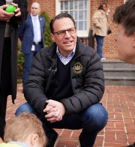 Photograph of Governor Shapiro crouching down talking to children on a sunny day. 