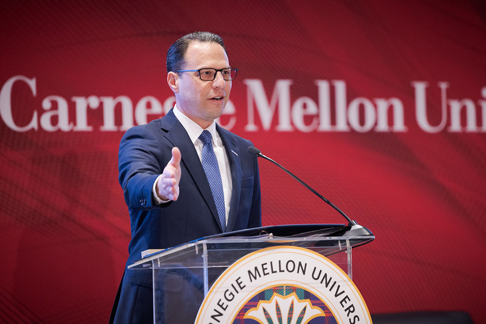 A photograph of Governor Shapiro standing at a podium speaking to a crowd at Carnegie Mellon University. 